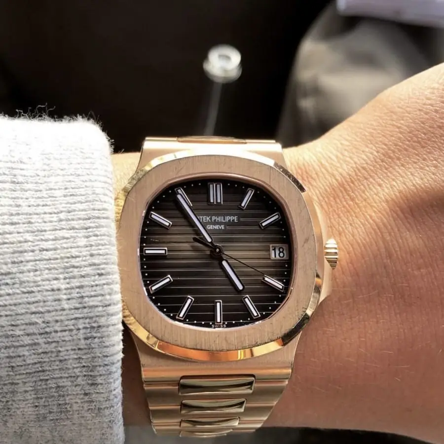 A gold watch on a wrist, half under a sleeve