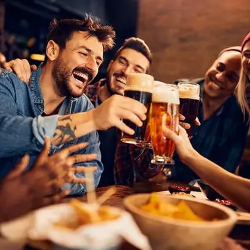 Friends raising beer glasses together at a table in a pub