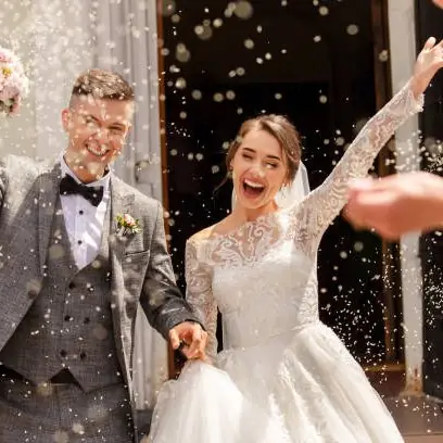 A newlywed couple stepping outside, laughing, under a shower of rice